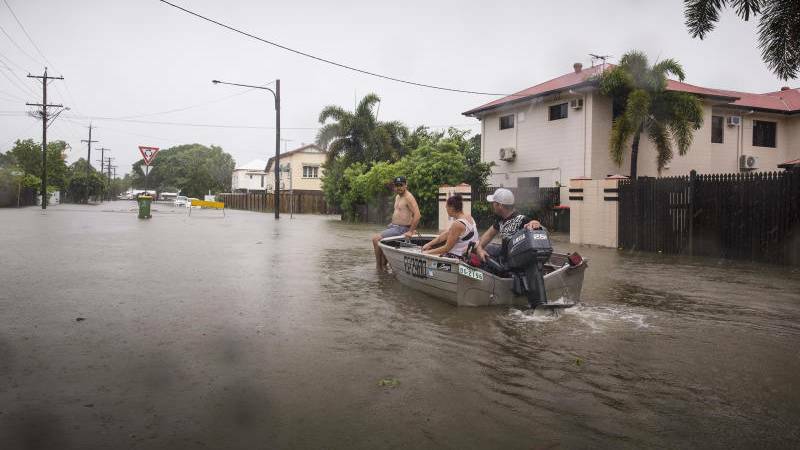 RELIEF: Rosslea residents Stephen Jubbs, Stacie Little and Stephen Dobbs take their boat around floodwaters in Rosslea, Townsville, on Saturday. Photos: AAP